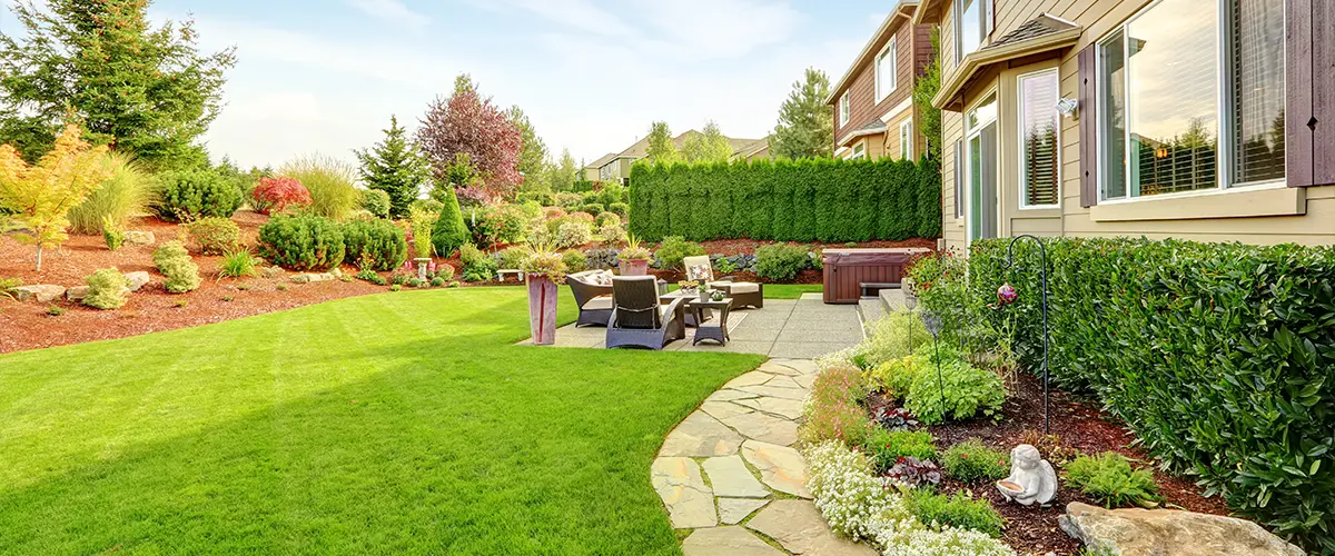 Backyard with vibrant landscaping, stone pathway, and a cozy patio seating area surrounded by greenery.