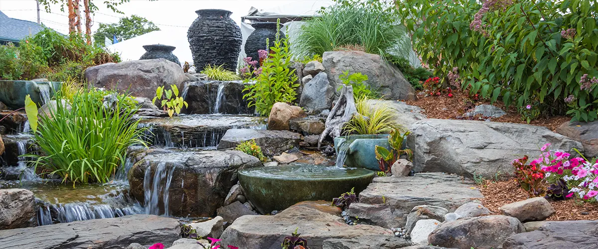 Beautiful garden waterfall with vibrant flowers and lush greenery, featuring natural rocks and cascading water.