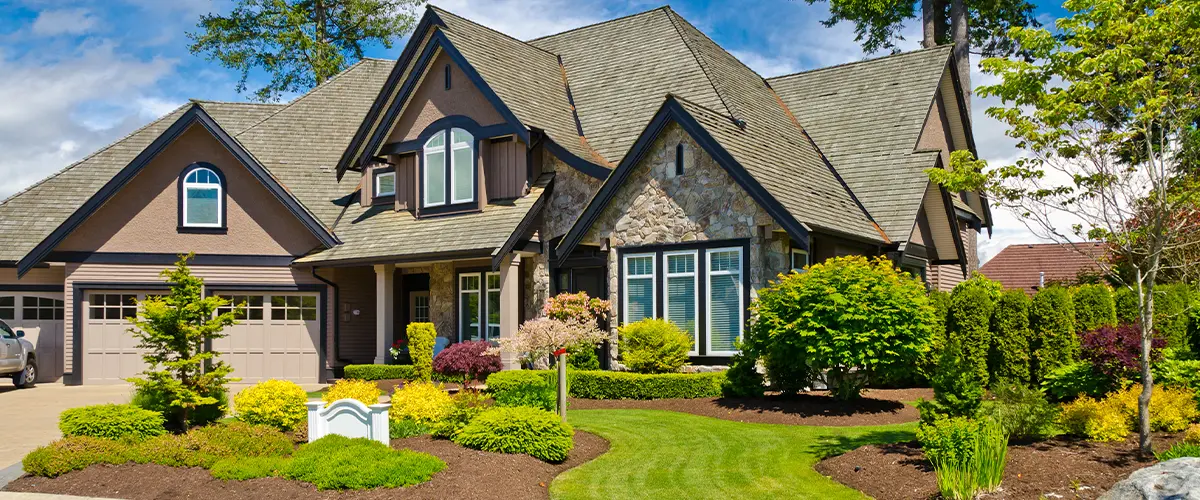 Beautiful stone-front home with lush landscaping and manicured lawn under a clear blue sky.