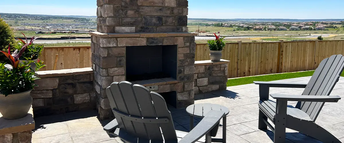 Stone outdoor fireplace with Adirondack chairs and scenic backyard views, designed for relaxing outdoor living.