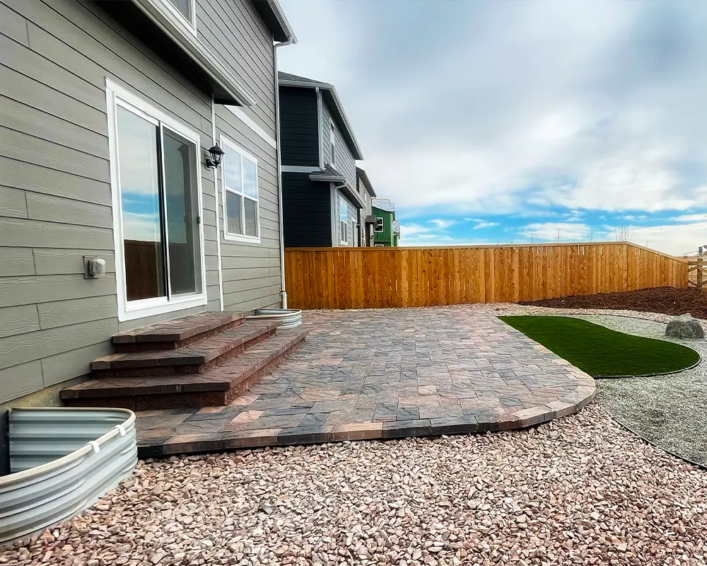 Modern backyard patio with multi-level stone pavers and privacy fence, ideal for outdoor relaxation and gatherings.