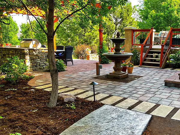 Paver patio with fountain and lush landscaping by Easy Green Landscaping.