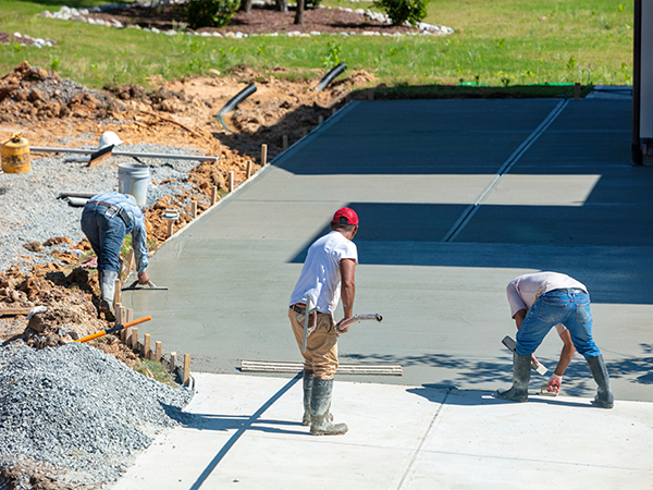 Workers leveling concrete driveway for durable, smooth finish on residential property.