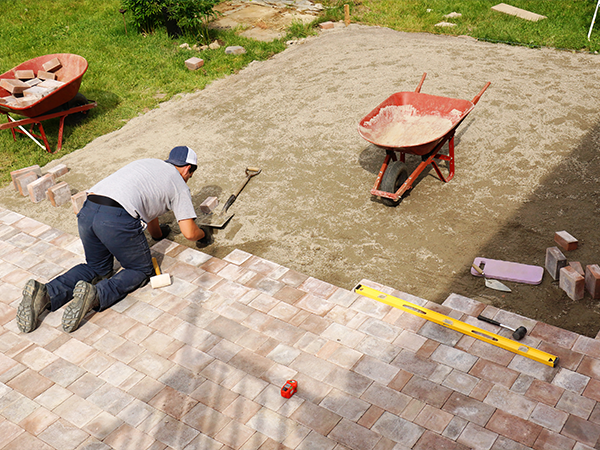 Worker installing paver stones for backyard patio, using tools for precise alignment.