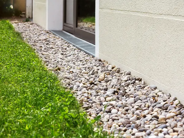 Gravel-filled drainage along house wall to prevent water damage and enhance yard drainage efficiency.