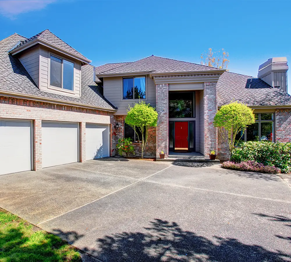 Large concrete driveway and entrance of a brick home with manicured trees and shrubs for enhanced curb appeal.