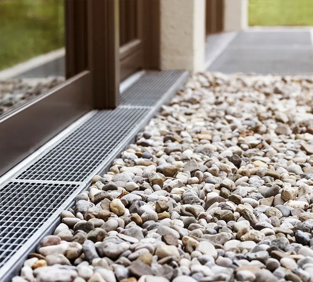 Close-up of French drain grate with surrounding rocks for efficient water flow management.